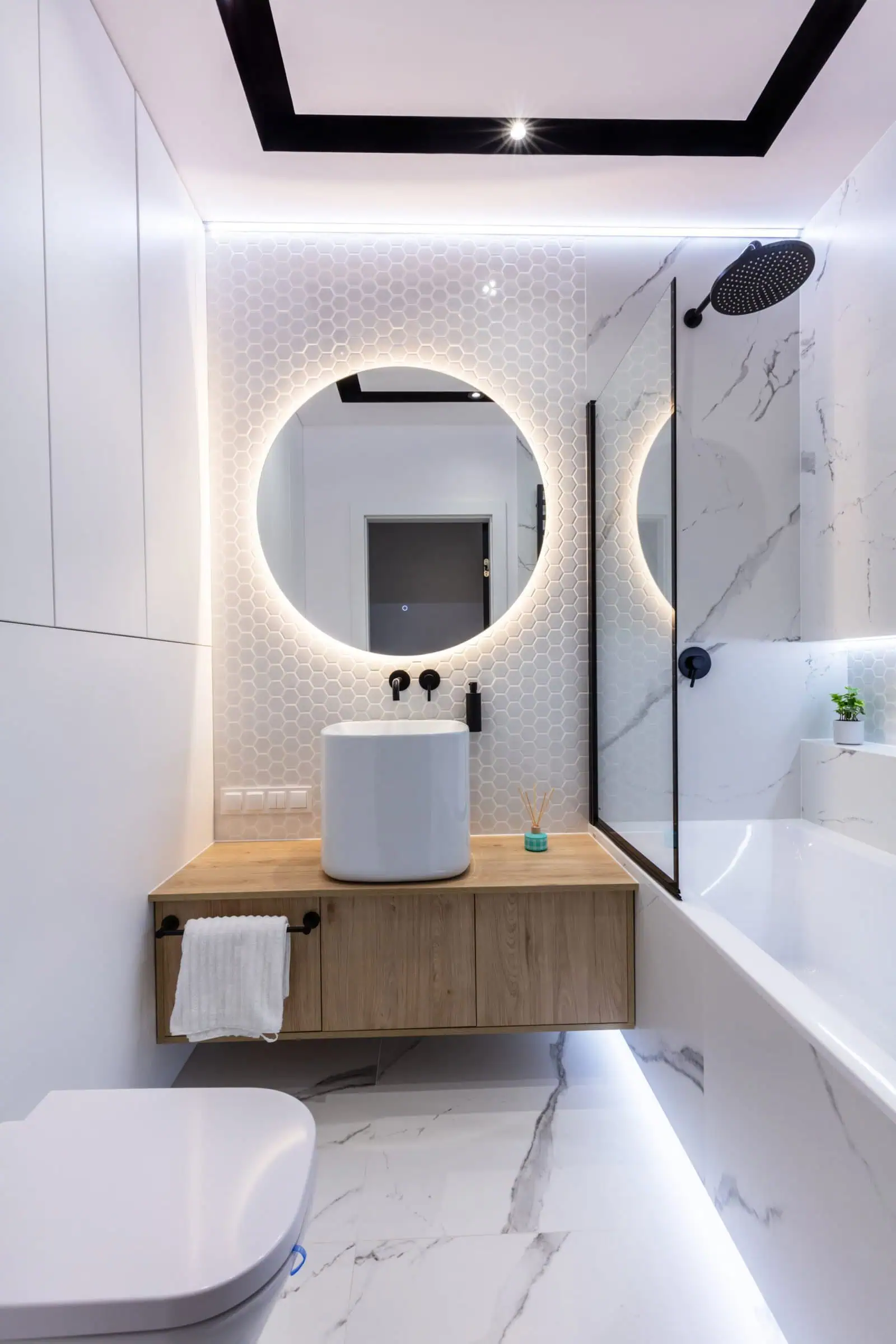 Modern bathroom with round illuminated mirror, vessel sink, and walk-in shower.